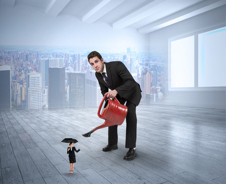 Businessman watering tiny businesswoman against city scene in a roomの写真素材