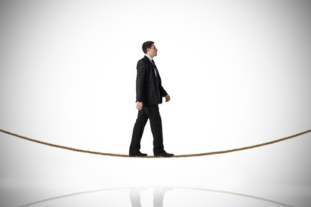 Handsome businessman stepping on tightrope against white background with vignetteの写真素材