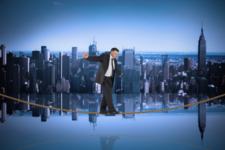 Mature businessman doing a balancing act on tightrope against mirror image of city skylineの写真素材