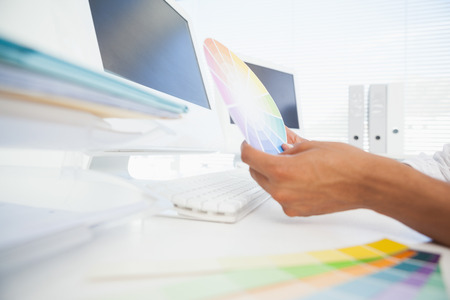 Designer working at desk holding colour wheel in his officeの写真素材