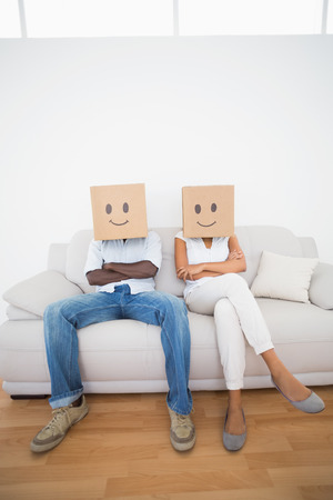 Couple sitting on couch together with boxes over head at home in the living roomの写真素材
