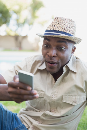Smiling man relaxing in his garden texting on phone on a sunny dayの写真素材