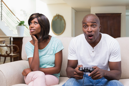 Bored woman sitting next to her boyfriend playing video games at home in the living roomの写真素材