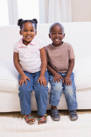 Happy siblings smiling at camera together at home in the living roomの写真素材