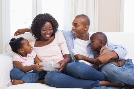 Happy family on the couch giving mother presents at home in the living roomの写真素材