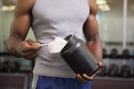 Mid section of a body builder holding a scoop of protein mix in gym