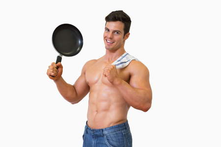 Portrait of a shirtless muscular man holding frying pan over white backgroundの写真素材