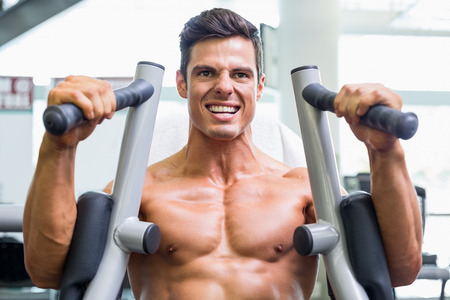 Determined young muscular man working on fitness machine at the gym