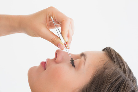 Close-up side view of hand plucking eyelashes over white background