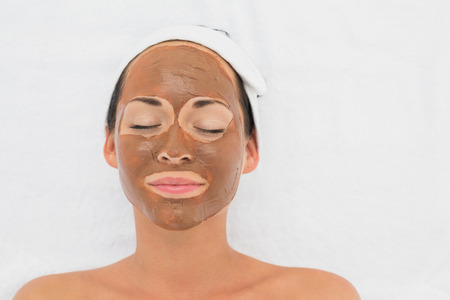 Smiling brunette getting a mud treatment facial in the health spaの写真素材
