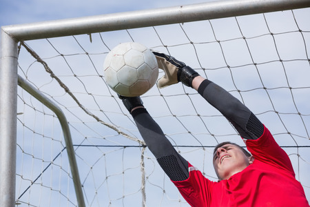 Goalkeeper in red jumping up to save a goal on a clear dayの写真素材