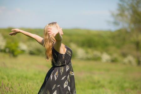 Pretty blonde in sundress standing with arms out on a sunny day in the countrysideの写真素材