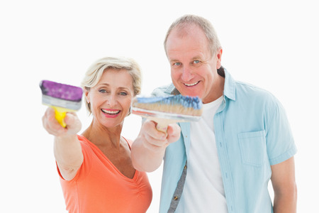 Happy older couple holding paintbrushes on white backgroundの写真素材