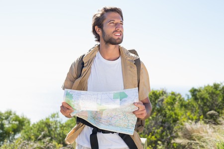 Handsome hiker holding map on mountain trail on a sunny day