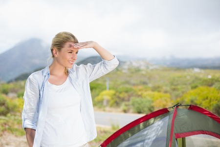 Attractive blonde standing by tent looking around on a sunny dayの写真素材
