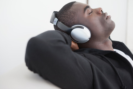 Casual man sitting on sofa enjoying music with eyes closed at home in the living roomの写真素材
