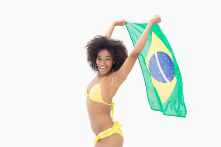 Athletic girl in yellow bikini holding brazil flag on white backgroundの写真素材
