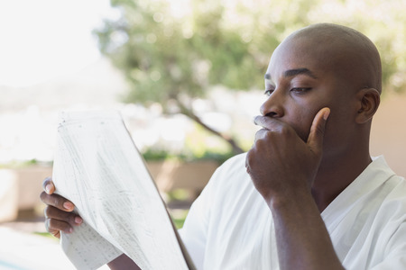 Handsome man in bathrobe reading newspaper outside on a sunny dayの写真素材