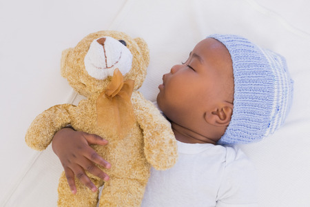 Adorable baby boy sleeping peacefully with teddy at home in the living room