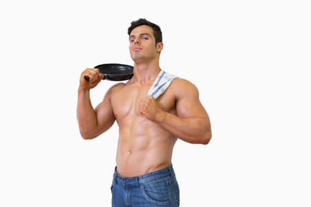 Portrait of a shirtless muscular man holding frying pan over white backgroundの写真素材