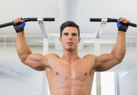 Shirtless male body builder doing pull ups at the gym
