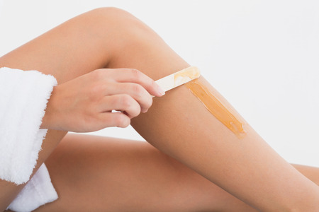 Close up side view of female applying hot wax on leg at spa centerの写真素材