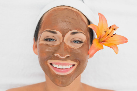 Smiling brunette getting a mud treatment facial in the health spaの写真素材