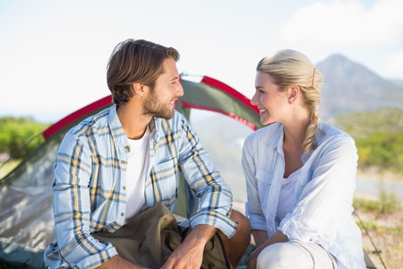 Attractive hiking couple smiling at each other outside their tent on a sunny dayの写真素材