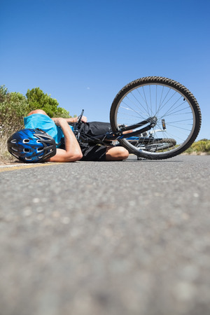 Cyclist lying on the road after an accident on a sunny dayの写真素材