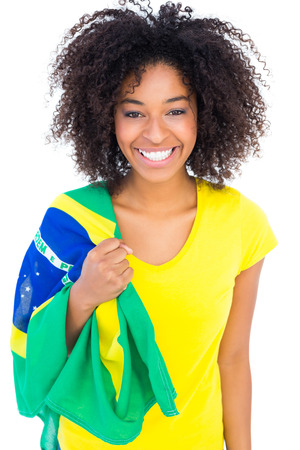 Pretty girl in yellow tshirt holding brazilian flag smiling at camera on white backgroundの写真素材