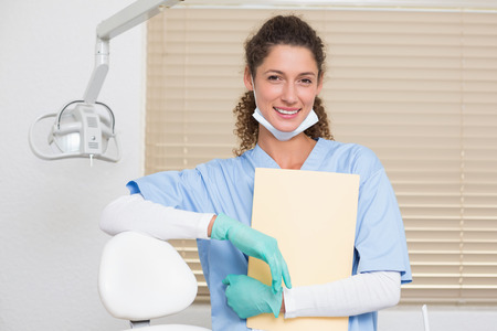 Dentist in blue scrubs smiling at camera holding file at the dental clinicの写真素材