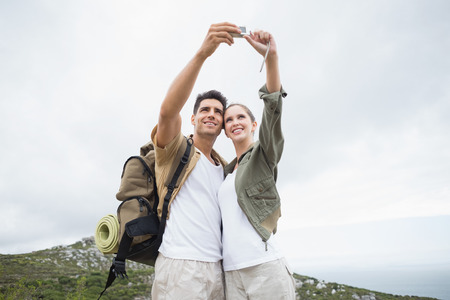 Happy hiking young couple taking picture of themselves on mountain terrainの写真素材