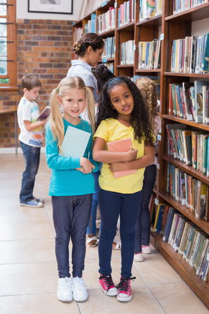 Cute pupils and teacher looking for books in library at the elementary schoolの写真素材