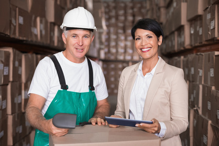 Warehouse worker scanning box with manager holding tablet pc in a large warehouseの写真素材