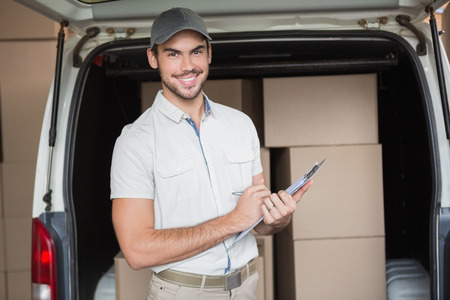 Delivery driver smiling at camera beside his van in a large warehouseの写真素材