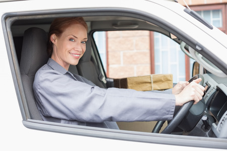 Delivery driver smiling at camera in her van outside the warehouse