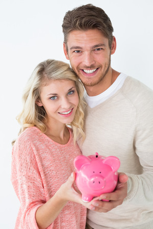 Portrait of attractive young couple holding piggybank over white backgroundの写真素材