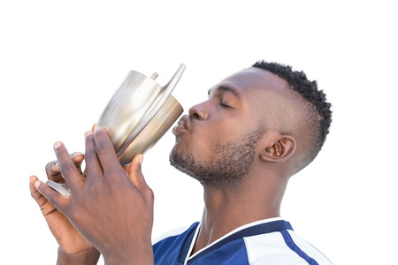 Football player kissing winners cup over white background