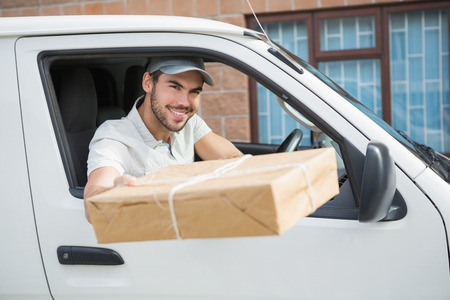 Delivery driver offering parcel from his van outside the warehouseの写真素材