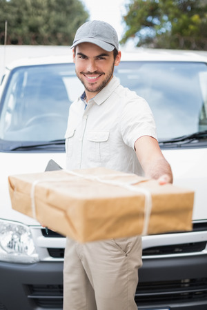 Delivery driver smiling at camera by his van offering parcel outside the warehouseの写真素材