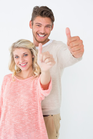 Portrait of happy young couple gesturing thumbs up over white backgroundの写真素材