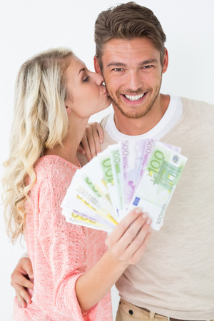Young woman kissing man as she holds banknotes over white backgroundの写真素材
