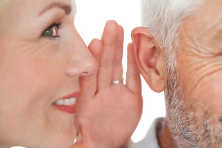 Close up of a woman whispering secret into a man's ear over white background