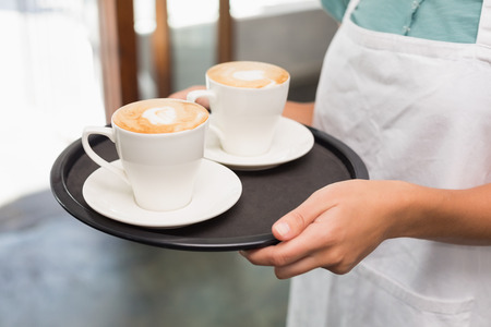 Waitress holding tray with cappuccinos at the coffee shopの写真素材