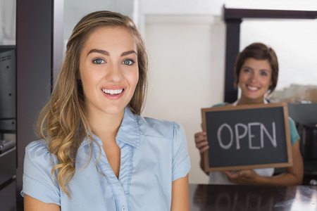 Pretty waitress and customer smiling at camera at the coffee shopの写真素材