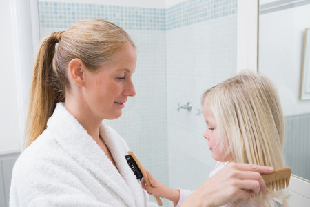 Happy mother and daughter brushing hair at home in the bathroomの写真素材