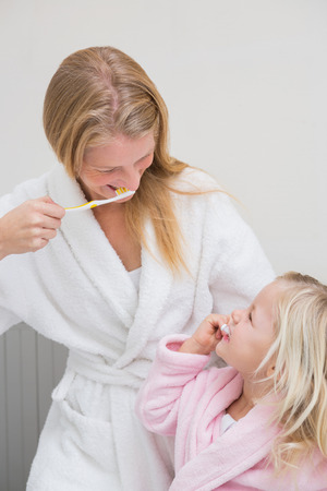 Happy mother and daughter brushing their teeth at home in the bathroomの写真素材