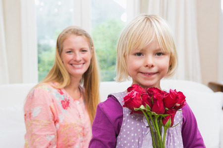 Happy woman holding red roses with daughter at home in the living roomの写真素材