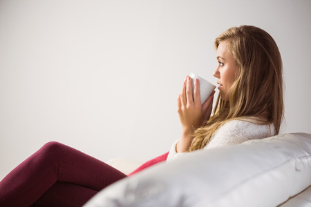 Pretty blonde relaxing on the couch with tea at home in the living roomの写真素材