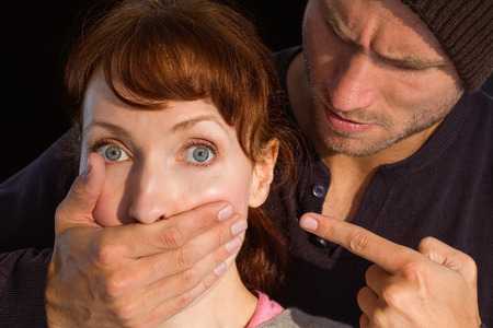 Man grabbing woman around mouth on black backgroundの写真素材